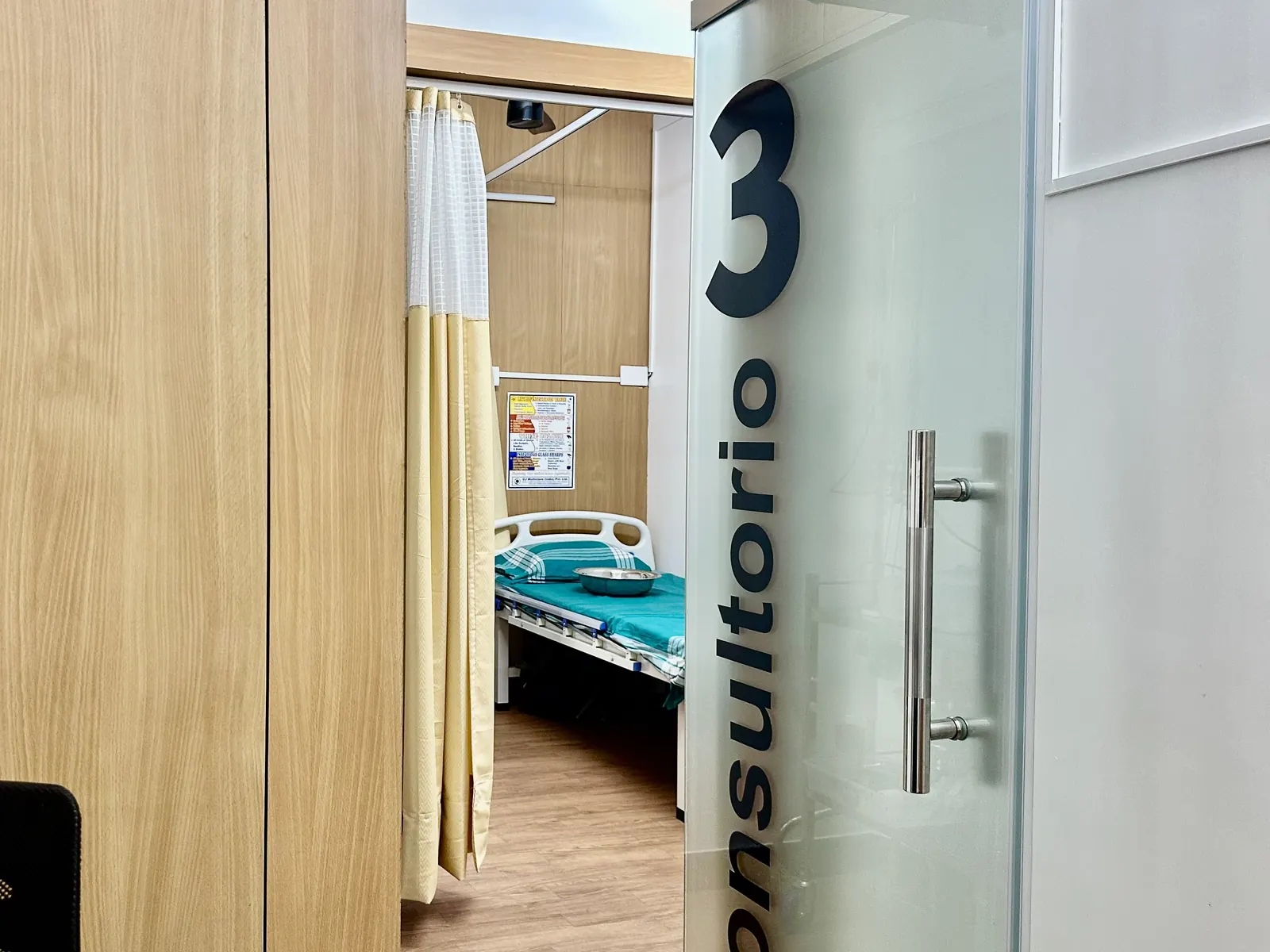 Treatment room with a patient bed and privacy curtain, seen through the consultation room door